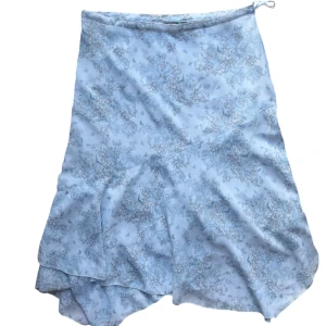 Vintage Ljusblå blommig volang asymmetrisk kjol - Blå maxi kjol med mönster. Har pärlor på sig. Strl 42 men mer en S-M i storlek. Knäppning och dragkedja på sidan. 