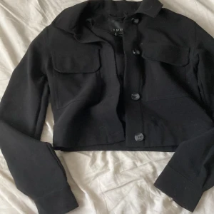 Svart jacka från Amisu - Säljer en svart jacka från Amisu med stora bröstfickor och knäppning framtill. Jackan har lång ärm och klassisk krage, perfekt för en trendig look. Passar dig som gillar stilrena och enkla plagg.