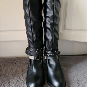 ,Stövlar, Svart, strl 39 - Oanvända Ett par svarta stövlar med dekorativa remmar och strassdetaljer. Perfekt för att ge din outfit en edgy touch. Strl 39 men små i storlek så passar mer någon som har strl 38. Nypris 999 kr . Köpta på lightinthebox. Klackhöjd ca 8 cm