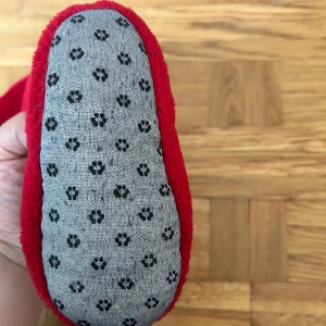 Röda tofflor med tomtemotiv - Mysiga röda tofflor med broderad tomte på ovansidan och halkskydd med tassmönster under sulan. Perfekta för kalla dagar inomhus och ger julkänsla direkt.