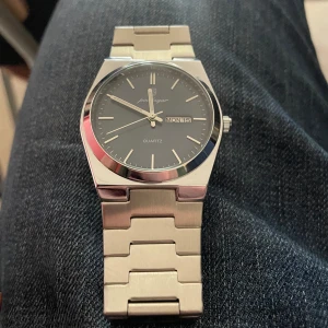 Silverfärgad klocka  - Snygg silverfärgad klocka med kvartsurverk. Den har en stilren mörkblå urtavla med dag- och datumvisning. Armbandet är i rostfritt stål och ger en elegant look. Perfekt för den som gillar en klassisk stil. PRIS KAN DISKUTERAS