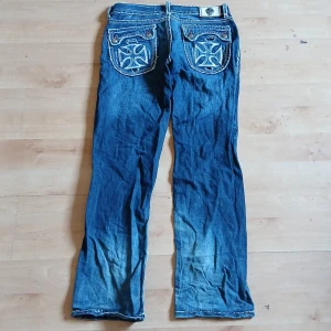 Laguna beach. Blå jeans med broderade bakfickor - Laguna beach   Säljer ett par blå jeans med unika broderade detaljer på bakfickorna och slitningar framtill. Jeansen har raka ben och kontrastsömmar längs kanterna. Perfekta för dig som gillar en lite mer edgy stil.