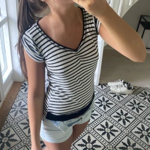 Randig topp med v-ringning - Säljer en svartvit randig topp med v-ringning och korta ärmar. Toppen har en tight passform och svarta detaljer vid ärmslut och nederkant. Perfekt för en stilren och enkel look. Hör av er vid frågor😊