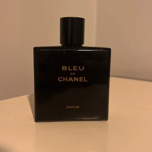 Bleu de Chanel Parfum 100 ml - Exklusiv herrparfym från Chanel, Bleu de Chanel Parfum i en elegant mörkblå glasflaska med guldtext. Flaskan rymmer ca 90-95 ml och har en stilren, fyrkantig design med svart lock. 