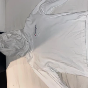 Vit hoodie från Champion - Säljer en vit hoodie från Champion med broderad logga på bröstet och stor logga på ryggen. Tröjan har huva och långa ärmar, perfekt för en avslappnad stil. Klassisk och enkel design som passar till det mesta.
