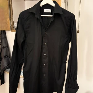 Svart skjorta från Eton - Svart slim skjorta från Eton i storlek 38. Endast använd ett fåtal gånger och håller mycket bra skick, nästan nyskick. Det bör tilläggas att materialet och kvaliteten är grym! Behöver knapps strykas!