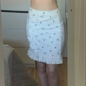 Blommig kjol  - Supersöt vit kjol från LMTD med små blå blommor och volangkant nertill samt volang vid omlotten🌸Aldrig använd!