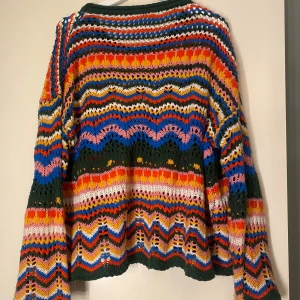 Färgglad stickad tröja med vågigt mönster - Säljer en unik och färgglad stickad tröja med vågigt mönster i grönt, blått, rosa, rött, orange, gult och vitt. Tröjan har lång ärm och en lös passform, perfekt för dig som gillar retrostil och vill sticka ut.