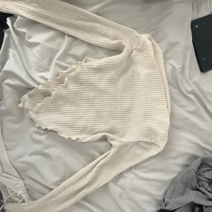 Vit ribbad topp från SHEIN - Säljer en vit ribbad topp från SHEIN i storlek XS. Tröjan har lång ärm och en unik vågig nederkant. Perfekt för dig som gillar stilrena och trendiga plagg med det lilla extra.