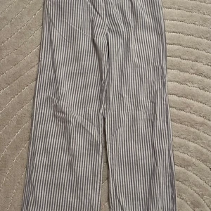 Randiga linnebyxor från H&M - Säljer ett par blå/gråvit randiga linnebyxor från H&M med elastisk midja. Byxorna har raka, vida ben och är tillverkade i ett lätt och luftigt material som passar perfekt för varmare dagar. Kolla min profil för fler kläder!