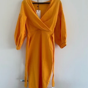 Boohoo orange klänning, storlek UK 8, helt ny med prislapp - Snygg och elegant klänning i en vacker orange färg. Klänningen har en v-ringning, puffärmar och en knut i midjan. Den är perfekt för en fest eller en kväll ute.  Helt ny med prislapp