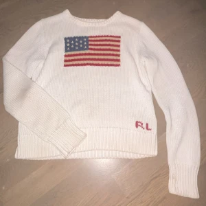 Polo Ralph Lauren tröja - Säljer en vit stickad tröja från Polo Ralph Lauren med amerikansk flagga på bröstet och RL-broderi nertill. Tröjan har lång ärm och rund halsringning. Perfekt för dig som gillar klassisk och stilren design. Storleken är 16 år men passar mig som vanligtvis har xs/s i tröjor