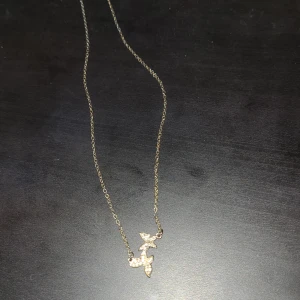 Guldigt halsband med fjärilar - Säljer ett tunt guldigt halsband med 2 små fjärilar dekorerade med glittriga stenar. Perfekt accessoar för att lyfta din outfit med en söt detalj.