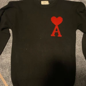 Svart stickad tröja från Ami Paris med rött hjärta - Svart stickad tröja från Ami Paris med ett rött hjärta och bokstaven A broderat på bröstet. Klassisk rund halsringning och långa ärmar. Perfekt för dig som gillar stilrena plagg med en twist. (Priset kan diskuteras)