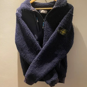 Mörkblå teddyjacka från Stone Island - Säljer en mörkblå teddyjacka från Stone Island med dragkedja och bröstficka. Jackan har lång ärm och klassisk patch på vänster ärm. Perfekt för kyliga dagar och riktigt skön att ha på sig. Kan ta byten 