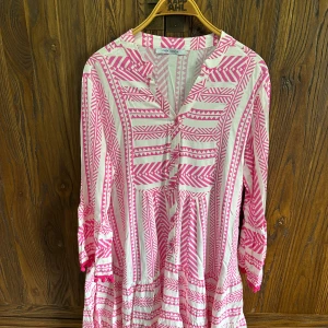 Vit och rosa mönstrad klänning - Säljer en luftig vit klänning med rosa grafiskt mönster. Klänningen har trekvartsärm och v-ringning framtill. Perfekt för varma dagar och har en avslappnad passform.