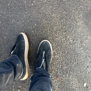 Axel Arigato Skor - Säljer ett par svarta sneakers från ARIGATO i mocka med vit platt sula och dragkedja framtill istället för klassisk snörning. Snygg minimalistisk design och diskret logga på sidan. Perfekta för dig som gillar stilrena skor med en twist. Säljs inte längre!