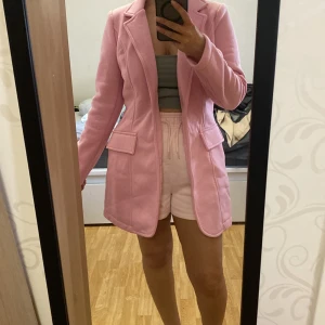 Ljusrosa kappa med fickor - Säljer en ljusrosa kappa med klassisk krage och två stora fickor framtill. Jackan har lång ärm och en rak, något längre passform som går ner över låren. Perfekt för dig som vill ha en färgglad och stilren jacka.