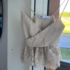Beige stickad linnetopp med spets från Zara - Supersöt beige linnetopp från Zara med smala axelband, omlott-detalj och volangig spets nertill. Toppen har knyt i ryggen och är perfekt för varma dagar. 