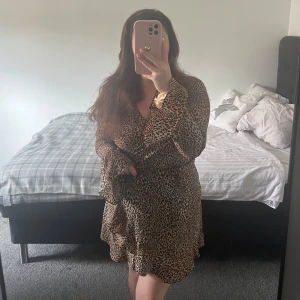 Leopardmönstrad omlottklänning - Säljer en snygg leopardmönstrad omlottklänning med volangdetaljer och knyt i midjan. Klänningen har långa ärmar och är i en kort modell, perfekt för dig som vill sticka ut lite extra. Superfin passform och skön att bära. 