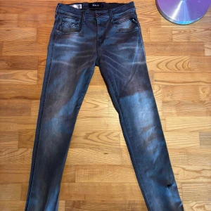 Replay jeans i tvättad blå färg - Säljer ett par Replay anbass jeans i tvättad grå färg med klassisk femficksdesign och raka ben. Midjemått W: 29 L: 30. Jeansen har en liten sliten detalj på ena benet. Perfekta för dig som gillar en avslappnad stil.