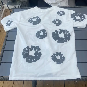 Vit t-shirt med svart mönster - Pris kan diskuteras Säljer en vit t-shirt från denim tears med unikt svart mönster över hela tröjan. T-shirten har rund hals och korta ärmar. Materialet är mjuk bomull och passformen är normal. Perfekt för dig som gillar streetwear med lite edge.