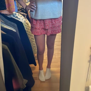 Röd blommig volangkjol från Zara - Supersöt röd kortkjol från Zara med blommigt mönster i vitt och svart. Kjolen har två volanger och resår i midjan för skön passform. Perfekt för dig som gillar färg och vill ha en lekfull look. Passar dig som är ca 13-14 år eller 164 cm men passar för mig som är 174cm och har S i midjan