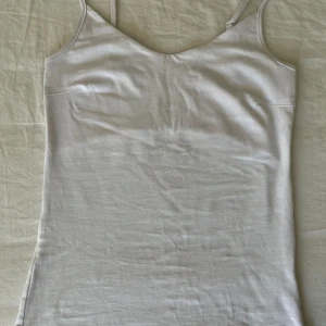 Vit linnetopp med smala axelband - Enkel och stilren vit linnetopp med smala, justerbara axelband och mjuk bomullskänsla. Perfekt att styla lager på lager eller bära som den är under varma dagar. Tidlös design med rak passform.