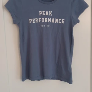 Blå Peak Performance t-shirt XS - Snygg blå t-shirt från Peak Performance i modellen PAULA TEE. XS, sann i storlek. Klassisk modell med vit text på bröstet. Tillverkad i mjuk bomull som är skön mot huden. Perfekt för dig som gillar sportiga och stilrena plagg💕