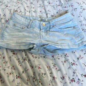 Ljusblå jeansshorts från i dodo XS - Supersnygga ljusblå jeansshorts från i dodo i storlek XS. Klassisk femficksmodell med silverfärgade nitar och detaljer på bakfickorna. Gjorda i stretchig bomullsmix för skön passform. Perfekta till sommaren och lätta att matcha med allt.