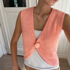 Stickad korallrosa väst Marc Lauge - Superfin stickad väst i korallrosa från Marc Lauge. Modellen har v-ringning, breda ribbade kanter och en stor matchande knapp framtill. Perfekt att styla över en t-shirt eller linne 💕Storlek M men passar Xs/S