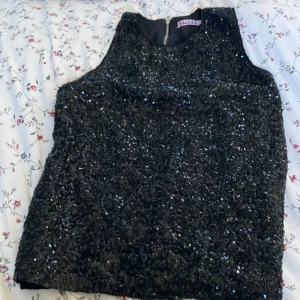 Svart paljettklänning från Skill - Säljer en svart kort paljettklänning från Skill, täckt med glittrande paljetter som ger en riktigt cool och festlig vibe. Klänningen är ärmlös och har en rak passform med dragkedja i ryggen. Perfekt för dig som vill sticka ut och glänsa!