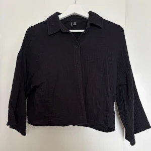 Svart skjorta från Vero Moda i linne - Svart skjorta från Vero Moda i luftig linneblandning. Skjortan har avslappnad passform, klassisk krage och knäppning framtill. Materialet är strukturerat och ger en cool, lite oversized vibe. Perfekt att styla med jeans eller kjol.