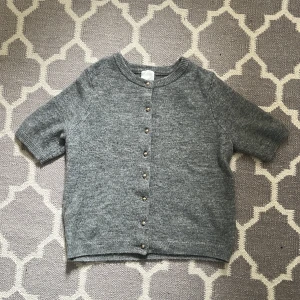 Grå kortärmad kofta från H&M - Säljer en grå kortärmad kofta från H&M med guldknappar. Den är i helt nytt skick då den knappt är använd💕