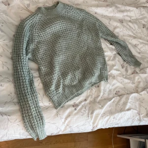 Ljusgrön stickad tröja från 157 - Supermysig ljusgrön stickad tröja från 157 med grovstickat mönster och hög ribbad krage. Tröjan har långärmade ärmar och en relaxed fit som passar perfekt till kyliga dagar. Enkel att styla med jeans eller kjol för en chill look.