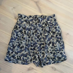 Blommiga shorts från Name It - Snygga högmidjade shorts från Name It i storlek 158.   De har justerbara band i midjan på båda sidorna. Endast annvända en gång. 