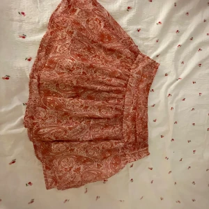 Röd paisleymönstrad kjol Gina Tricot - Supersöt kort kjol från Gina Tricot i röd och vit paisley. Kjolen har volang och resår i midjan för en bekväm passform. Tunt, luftigt tyg som passar perfekt till varmare dagar. Perfekt för dig som gillar boho-vibe och vill sticka ut lite extra.