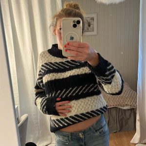 Randig stickad tröja i mörkblått och vitt - Säljer en mysig stickad tröja med breda diagonala ränder i mörkblått och vitt. Tröjan har en hög krage och långärmade ärmar, perfekt för kyliga dagar. Den har en loose passform och grovstickad struktur som ger en cool och avslappnad vibe. Från only I storlek L men passar dig med S,M själv är jag en S!