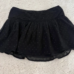 Svart prickig kjol från Gina Tricot - Supersöt svart kortkjol från Gina Tricot med små diskreta prickar och bred, veckad midja. Kjolen är lätt och luftig, perfekt för dig som gillar en enkel men ändå trendig look. Passar till allt och är riktigt skön att bära.