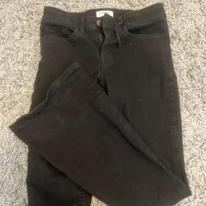 Svarta jeansbyxor från Lindex - Svarta jeansbyxor från Lindex i klassisk femficksmodell. Byxorna har hög midja, dragkedja och knapp framtill samt bälteshällor. Materialet är mjukt och stretchigt för en bekväm passform. Perfekta till sneakers eller boots.