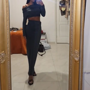 Mörkgrå lång kjol med offshoulder topp - Säljer en mörkgrå kjol med offshoulder topp med omlott-detalj i midjan. Settet har lång ärm och en croppad överdel som visar midjan. Materialet är mjukt och stretchigt, perfekt för dig som gillar en slim passform med lite edge.