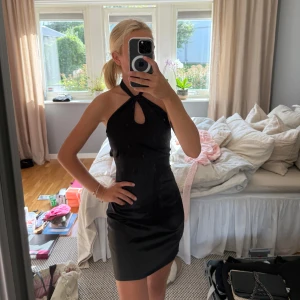 Svart klänning med knyt i ryggen - Säljer denna svarta klänningen med halterneck och snygg cutout framtill. Man knyter klänningen i ryggen och runt nacken. Helt i nyskick!