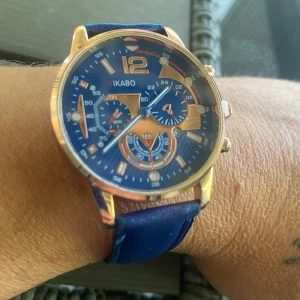 Blå och guldig klocka från Vikabo - Stilren klocka från Vikabo med blå urtavla och guldiga detaljer. Klockan har flera små urtavlor och ett blått armband i syntetmaterial. Snygg kombination av blått och guld som sticker ut på handleden.