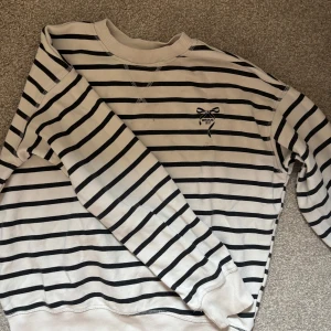 Randig sweatshirt Bisous 1921 XS - Vit och svart randig sweatshirt från Bisous 1921 i storlek XS. Tröjan har broderad rosett med logga på bröstet, rund hals och långa ärmar. Perfekt för en chill och stilren look.