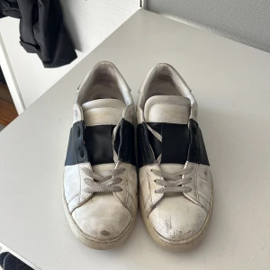 Valentino Garavani Open sneakers svart/vit - Snygga Valentino Garavani Open sneakers i vitt skinn med bred svart läderdetalj över vristen och coola nitar baktill. Klassisk rund tå, platt sula och snörning framtill. Perfekta för dig som gillar exklusiva och trendiga sneakers med edge. Säljer billigt pga rätt slitna men går bra att använda. Hålen i sulorna märks inte av vid användning! Kom med prisförslag och frågor😁