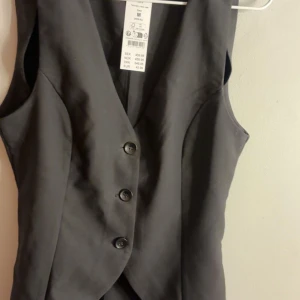 Svart skräddarsydd väst Gina Tricot - Snygg svart skräddarsydd väst från Gina Tricot med figurnära passform och tre knappar framtill. Västen har en längre, elegant skärning med spetsig nederkant och klassisk look. Perfekt att styla över en skjorta eller bara ha den som den är. Helt i nyskick med lapp och allt säljer då den är för liten för mig. Slutsåld överallt. Pris kan diskuteras