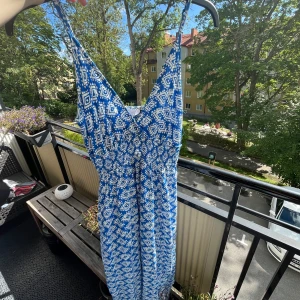 Blå och vit långklänning från Missguided - Säljer en snygg långklänning från Amisu med blått och vitt geometriskt mönster. Klänningen har smala axelband, v-ringad hals och smockad midja som ger en skön passform. Perfekt för varma dagar och sommarhäng! 