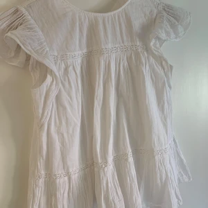 Vit blus i linne med spetsdetaljer - Superfin vit blus i linne med volangiga korta ärmar från Gina Young . Blusen har broderade spetsdetaljer och en luftig, flowy passform som känns perfekt för varma dagar. Materialet är lätt och svalt, och den har en romantisk vibe med sina fina detaljer. Den har en liten fläck där nere på framsidan (se sista bilden) men den syns knappt. Man knäpper blusen där bak med en knapp. 