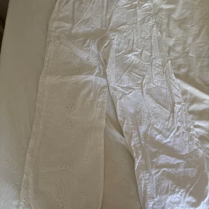 Vita broderade linne byxor från H&M - Säljer ett par vita byxor från H&M i storlek 152. Byxorna har ett broderat blommönster och är gjorda i bomull. De har elastisk midja för extra komfort och en rak passform som ger en chill vibe. Perfekta för varma dagar och en fräsch look.