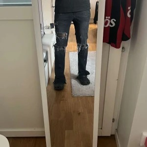 Svarta ripped jeans med bootcut - Säljer ett par svarta jeans med rejält slitna och trasiga detaljer vid knäna och låren. Byxorna har bootcut-snitt och sitter snyggt med normal passning. Perfekta för dig som gillar en edgy och avslappnad stil.